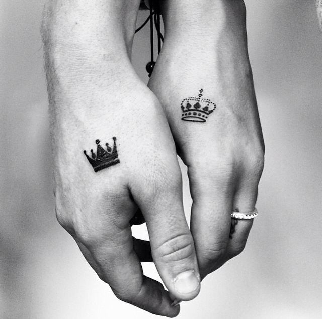 two people holding hands with tattoos on their fingers and one has a crown tattooed on the other