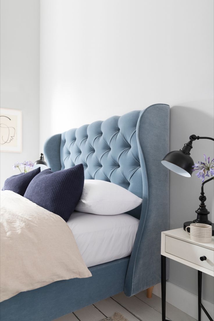 a bed with blue headboard and pillows in a white room next to a night stand