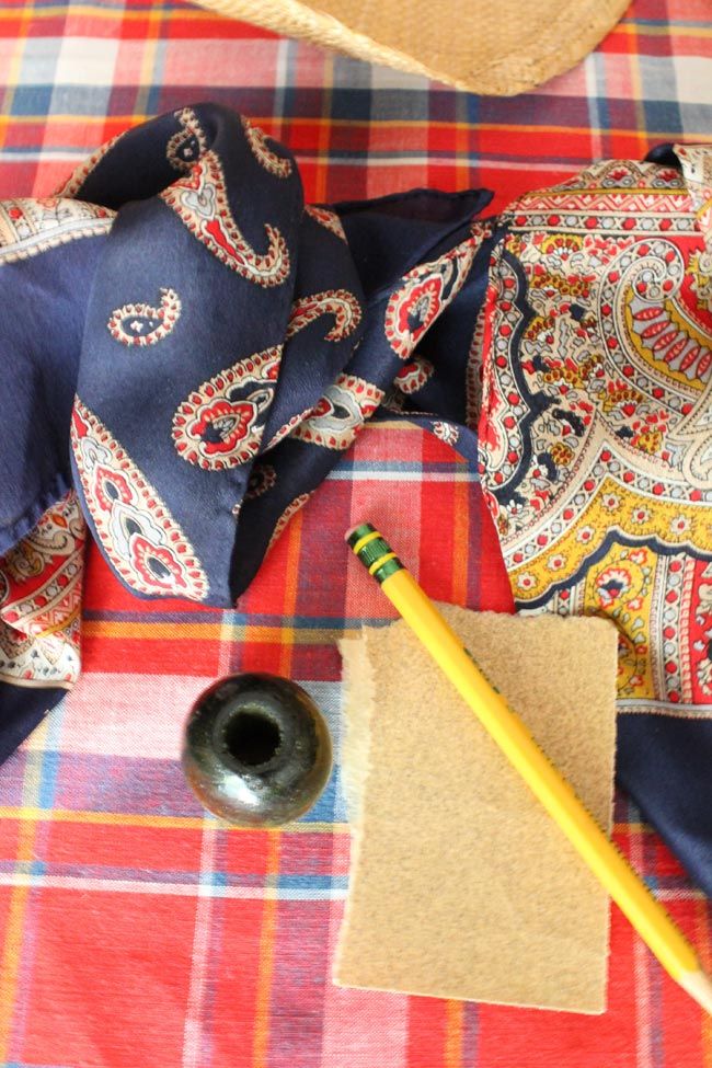 a hat, tie, and pen sitting on a plaid tablecloth with other items