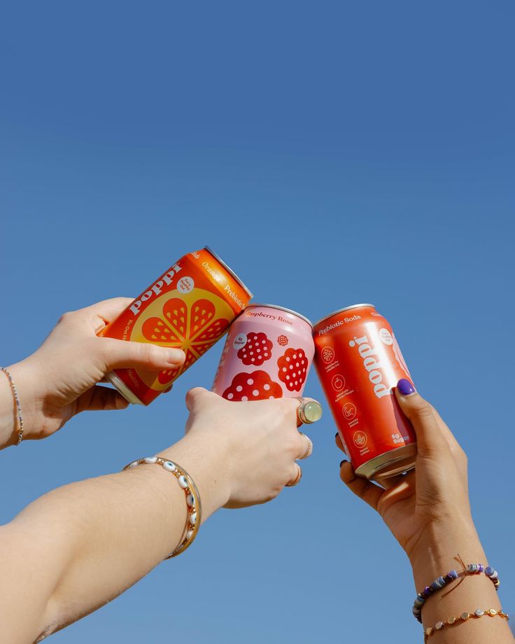 two women holding up cans of soda against a blue sky