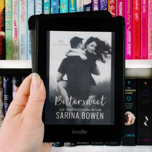 a person holding up a book in front of bookshelves with the cover pulled down