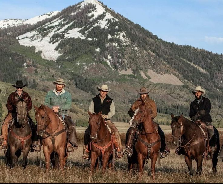 five men are riding horses in front of a mountain