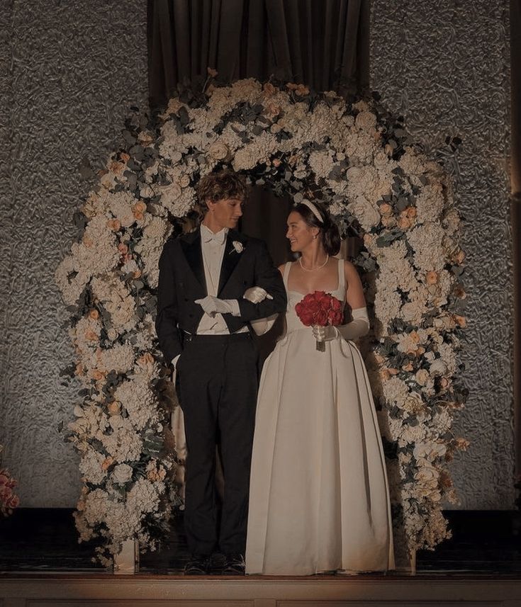 a bride and groom standing in front of a floral arch