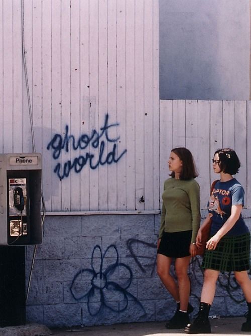 two girls walking past a wall with graffiti on it and a phone booth in the background