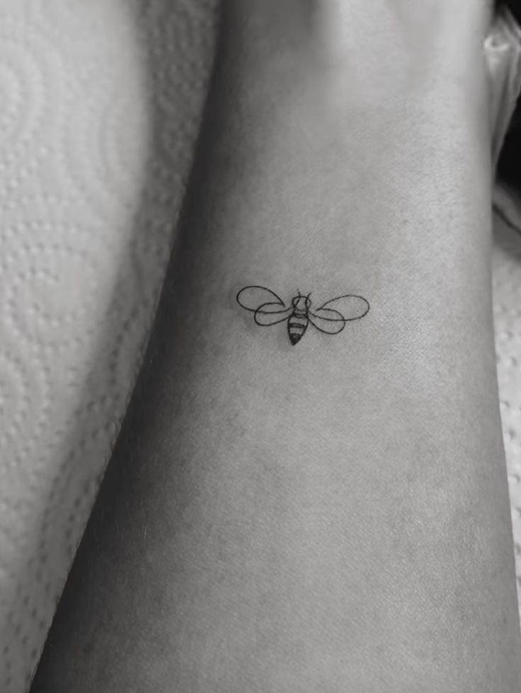 a black and white photo of a bee tattoo on the ankle, it looks like an insect