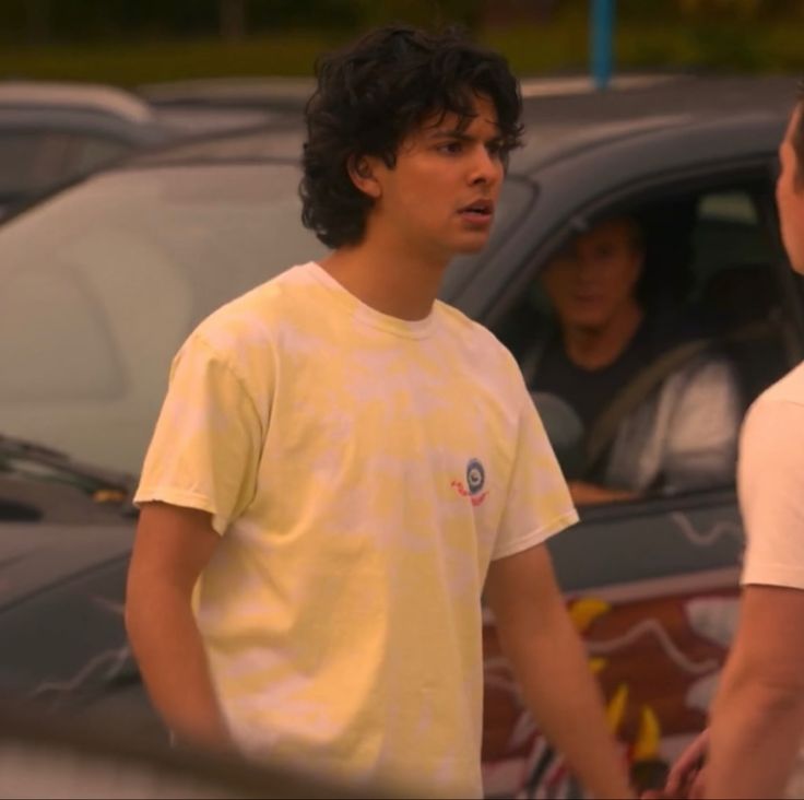 two young men standing next to each other in front of parked cars