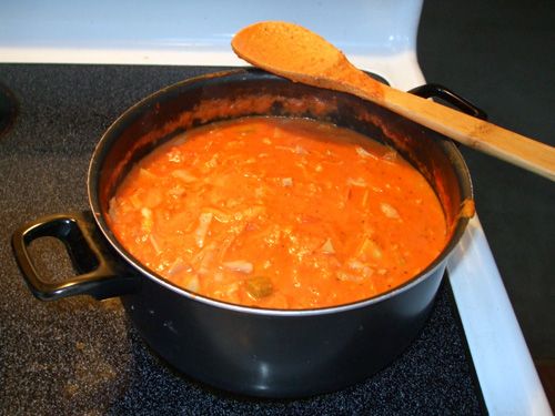 a large pot filled with food sitting on top of a stove next to a wooden spoon