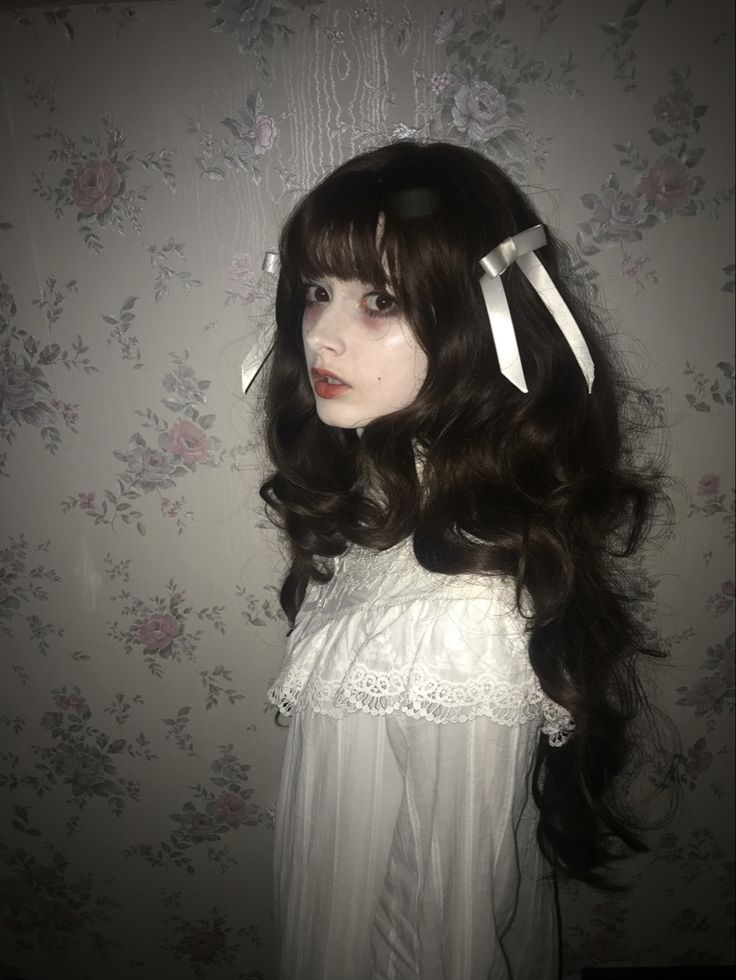 a woman with long black hair wearing white headbands in front of floral wallpaper