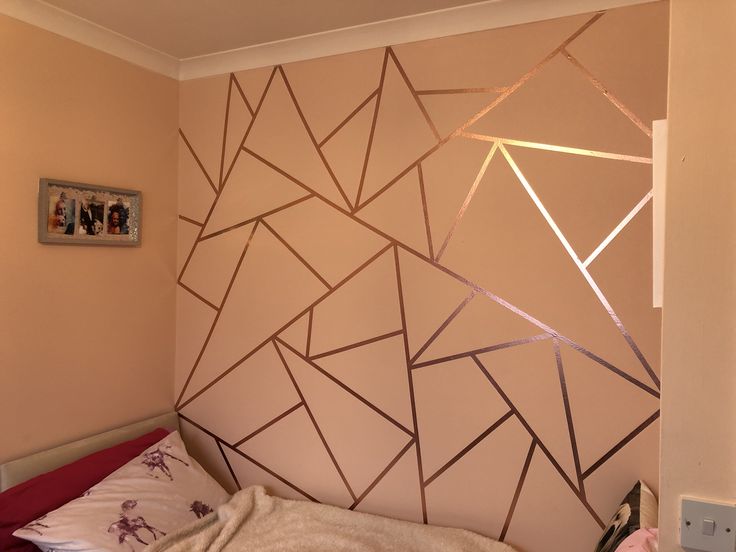 a bedroom with pink walls and gold foiled lines on the wall behind the bed