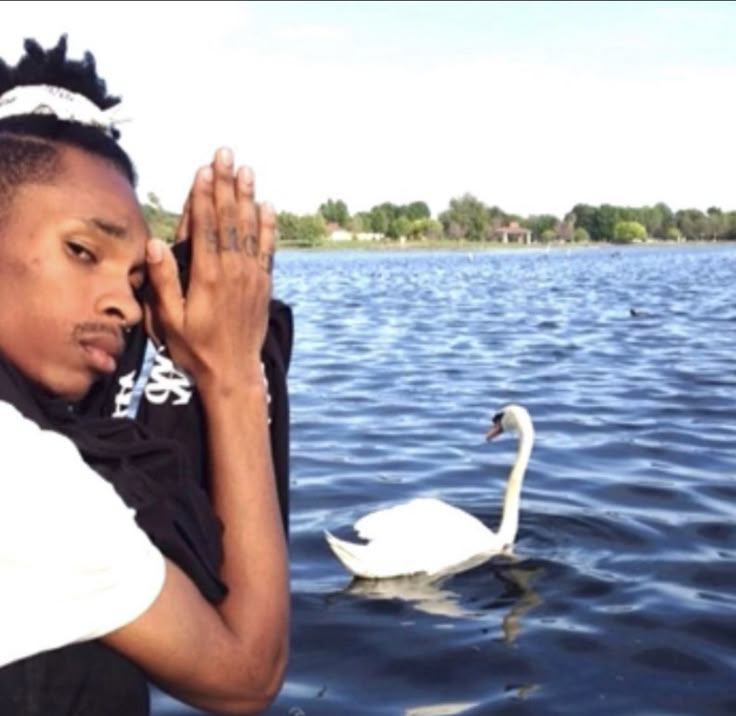 a woman standing next to a swan on top of a lake with her hands together