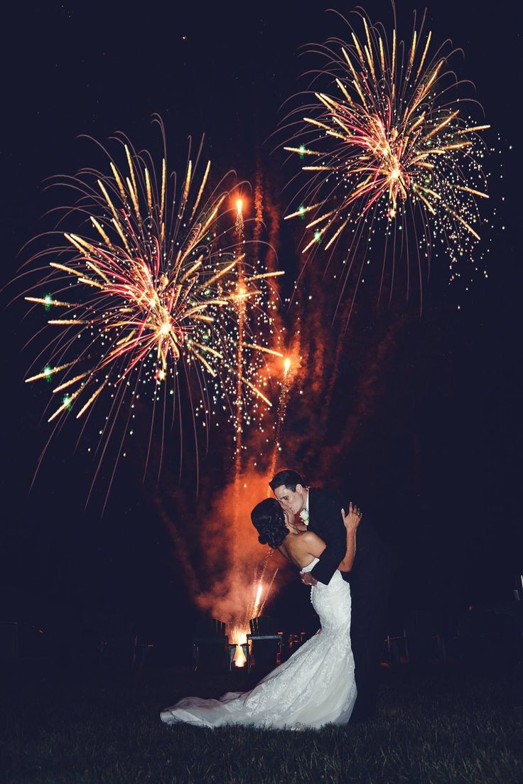 a bride and groom kissing in front of fireworks