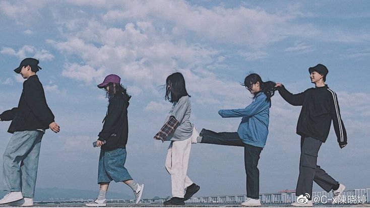 five young people are walking on the beach together, one is holding his leg up