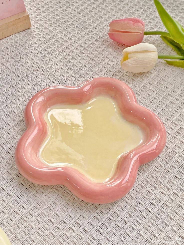 a pink flower shaped dish sitting on top of a table next to tulips