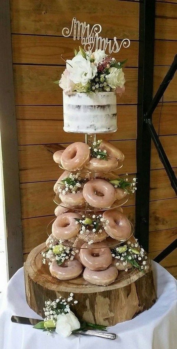 a wedding cake made out of doughnuts on top of a tree stump with flowers