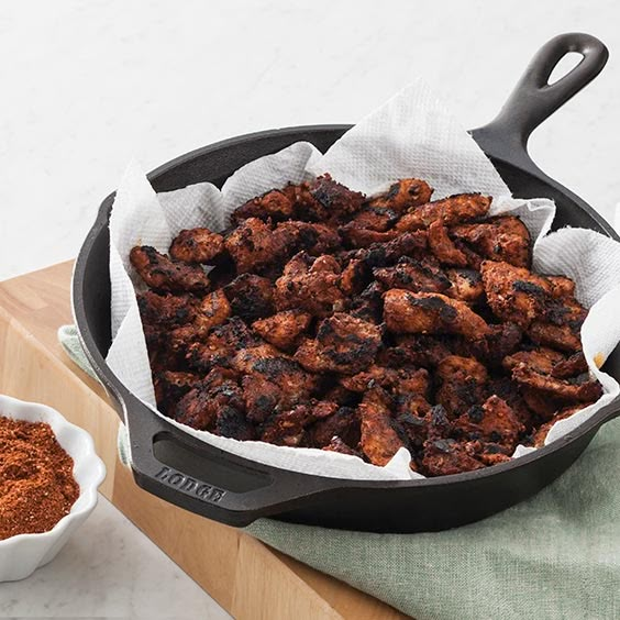 a pan filled with meat next to a bowl of seasoning on a cutting board