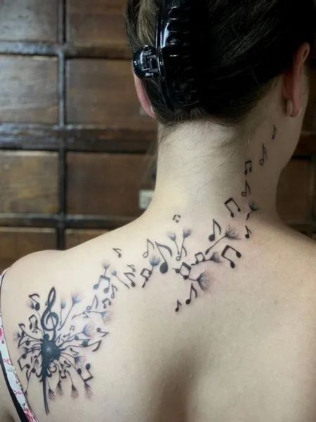 the back of a woman's neck with musical notes and flowers on her left shoulder