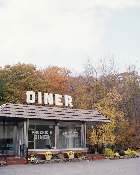 an old diner sits in the middle of a parking lot with autumn trees around it