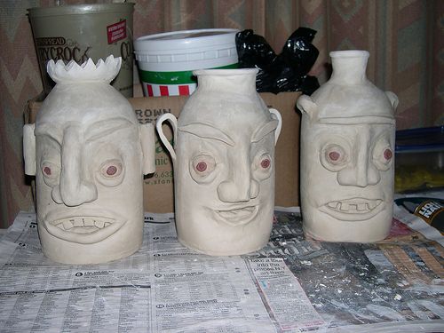 three ceramic jugs sitting on top of a table covered in papers and other items