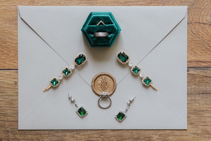 an envelope with rings and emeralds on it, next to a ring brooch