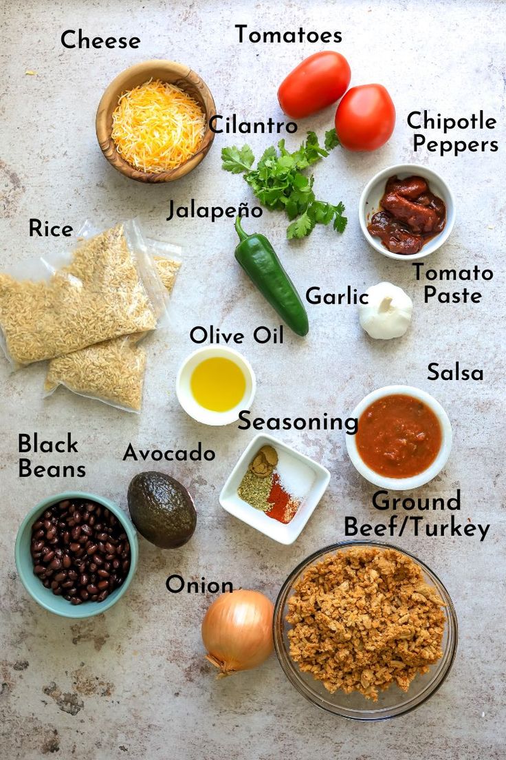 the ingredients for this mexican dish are laid out on a white surface with black beans, tomatoes, tortilla chips, cheese, jalapenos, guacamole peppers, and other condiments