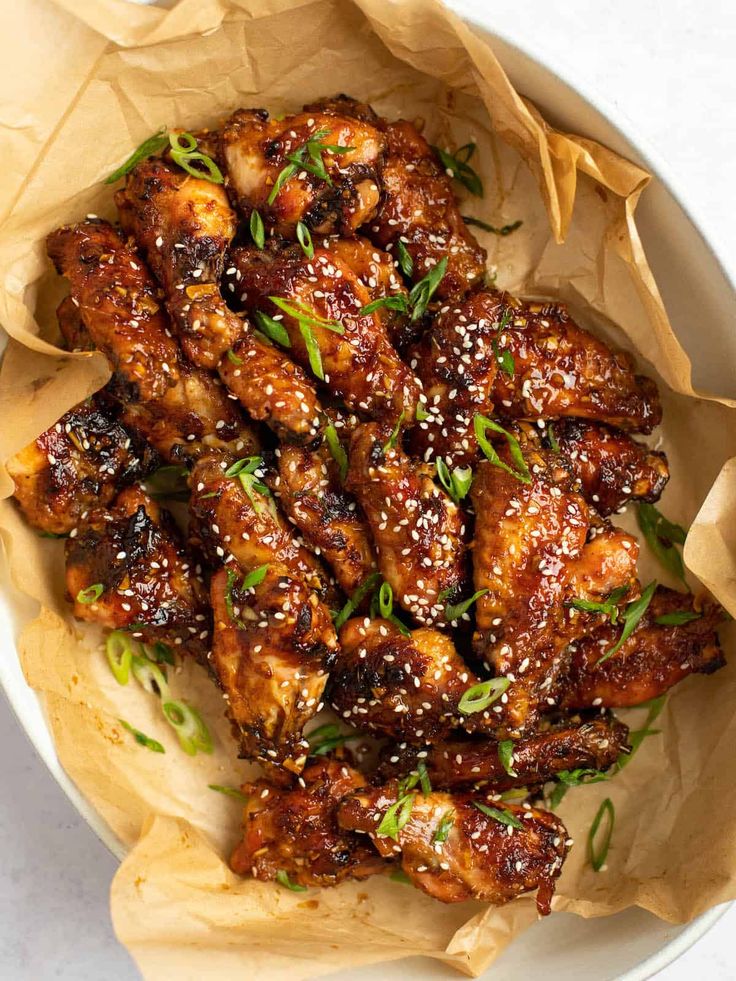 a white bowl filled with chicken wings covered in sesame seeds and garnished with green onions