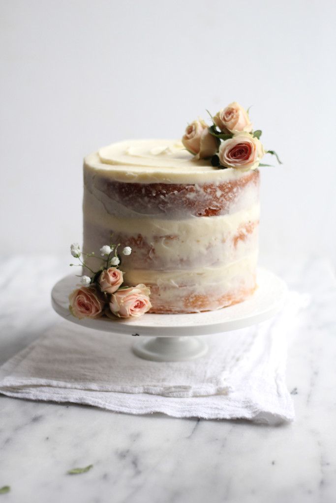 a three layer cake with white frosting and pink flowers on top, sitting on a plate