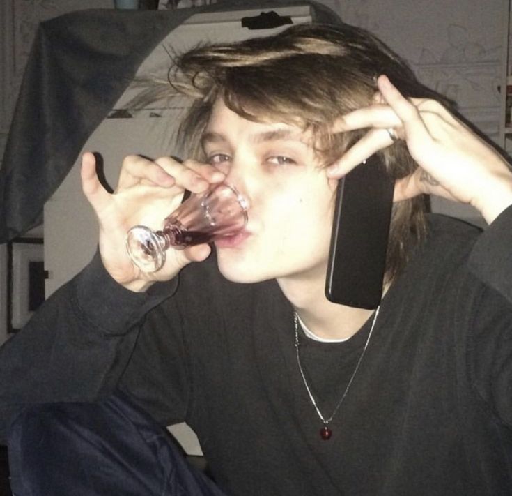 a young man drinking from a wine glass while talking on a cell phone