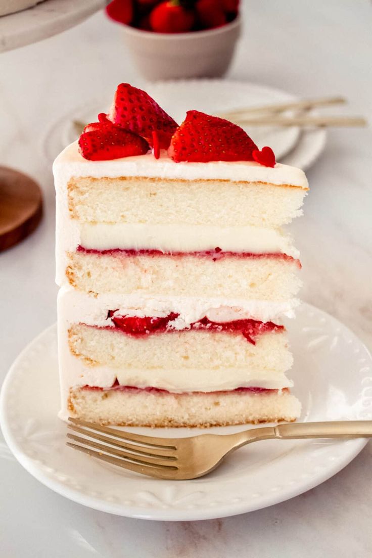 a slice of cake with strawberries on top and white frosting is sitting on a plate