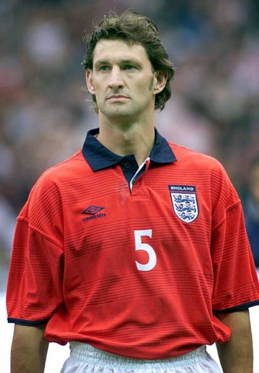 a man standing on top of a soccer field wearing a red shirt and white shorts