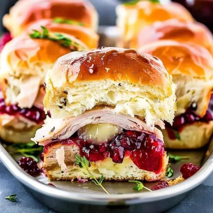 turkey and cranberry sandwich cut in half on a plate with other sandwiches behind it