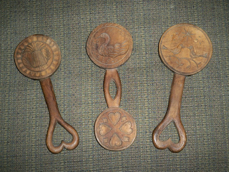 three old wooden spoons with handles on a green carpeted surface, one has an ornate design and the other has decorative designs