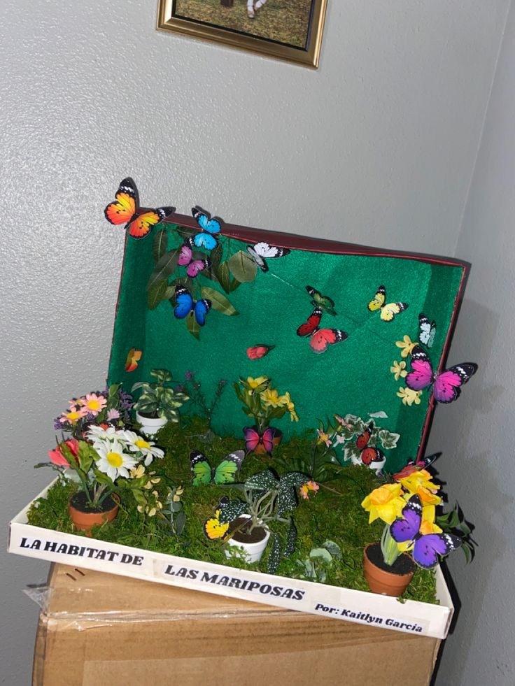 a box filled with lots of flowers and butterflies on top of a wooden table next to a painting