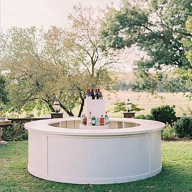 an outdoor bar with bottles on it in the middle of a lawn and some trees