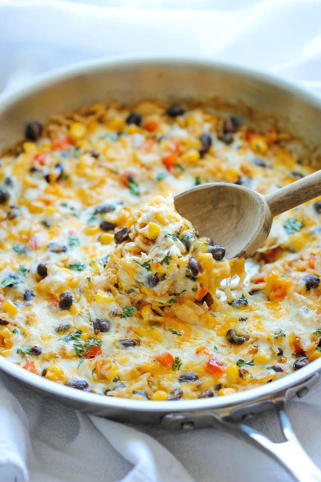 a casserole dish with cheese and black beans being stirred with a wooden spoon