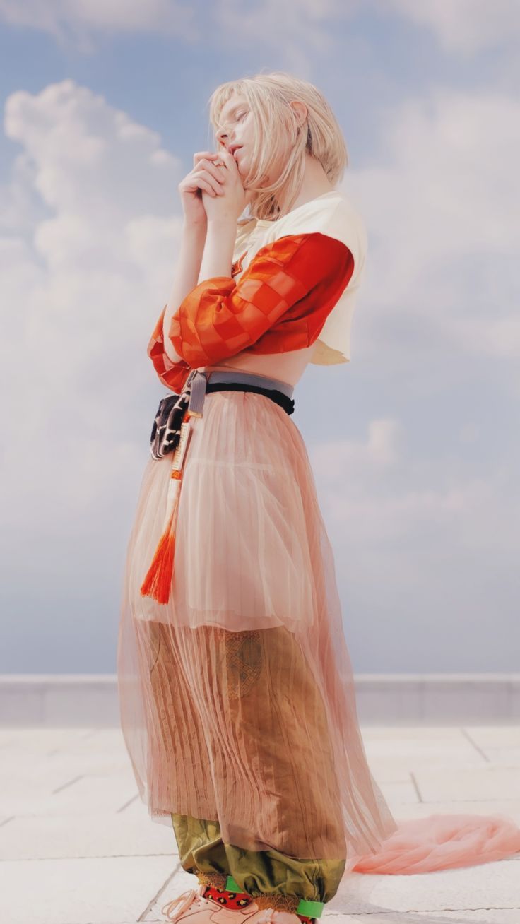 a woman in a long dress is standing on the ground with her hands to her face