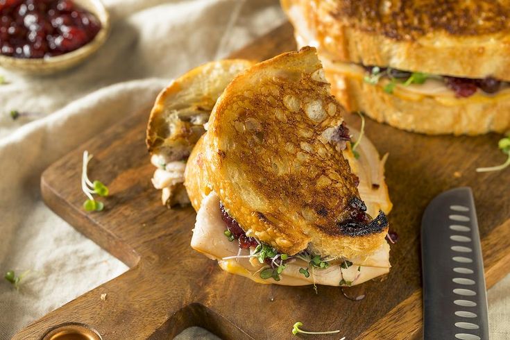 two sandwiches cut in half on a cutting board with a knife and cranberry sauce