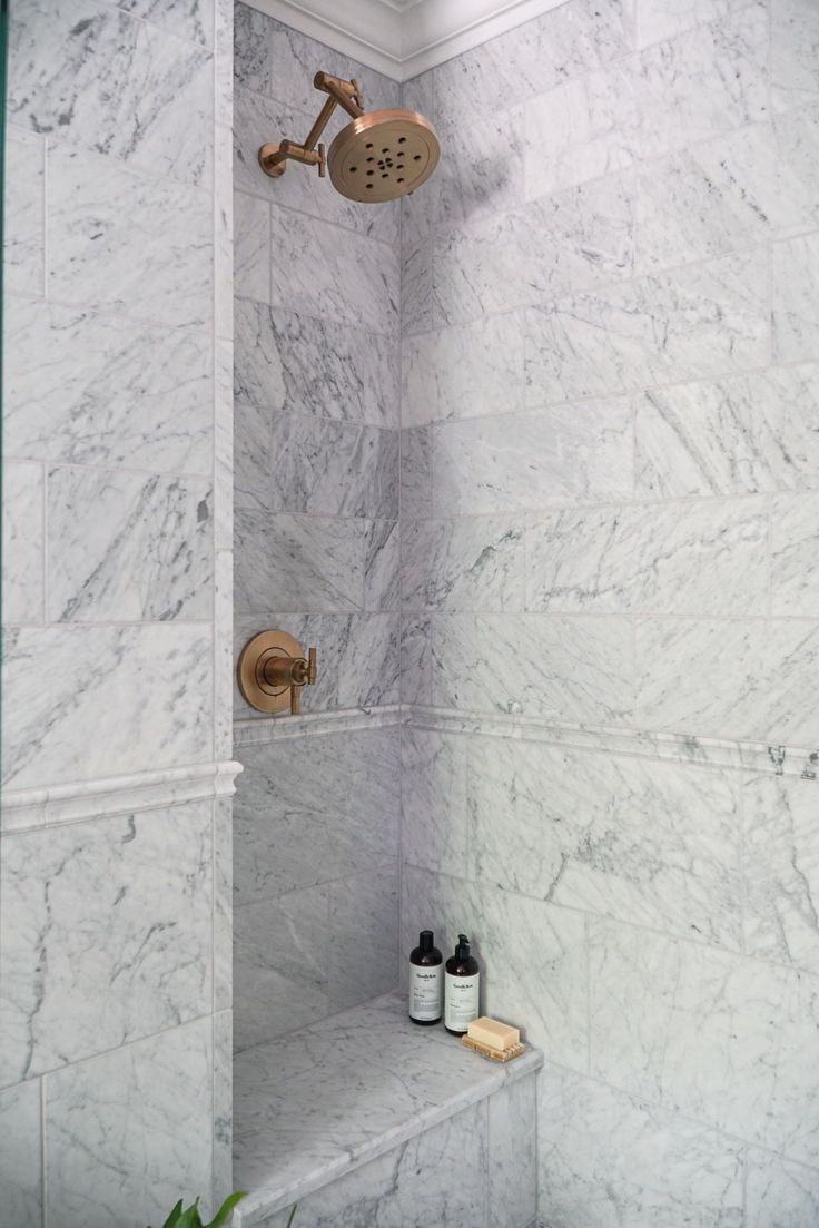 a bathroom with marble walls and floor, shower head and hand held faucet