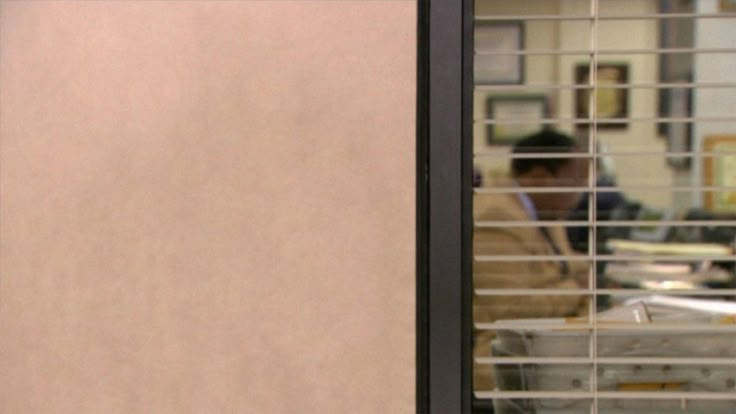 a man sitting at a table in front of a window with blinds on the outside