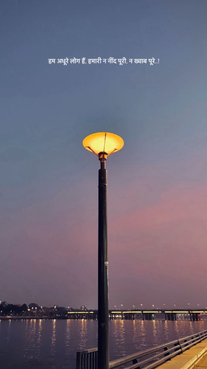 a street light sitting on the side of a river under a sky filled with clouds