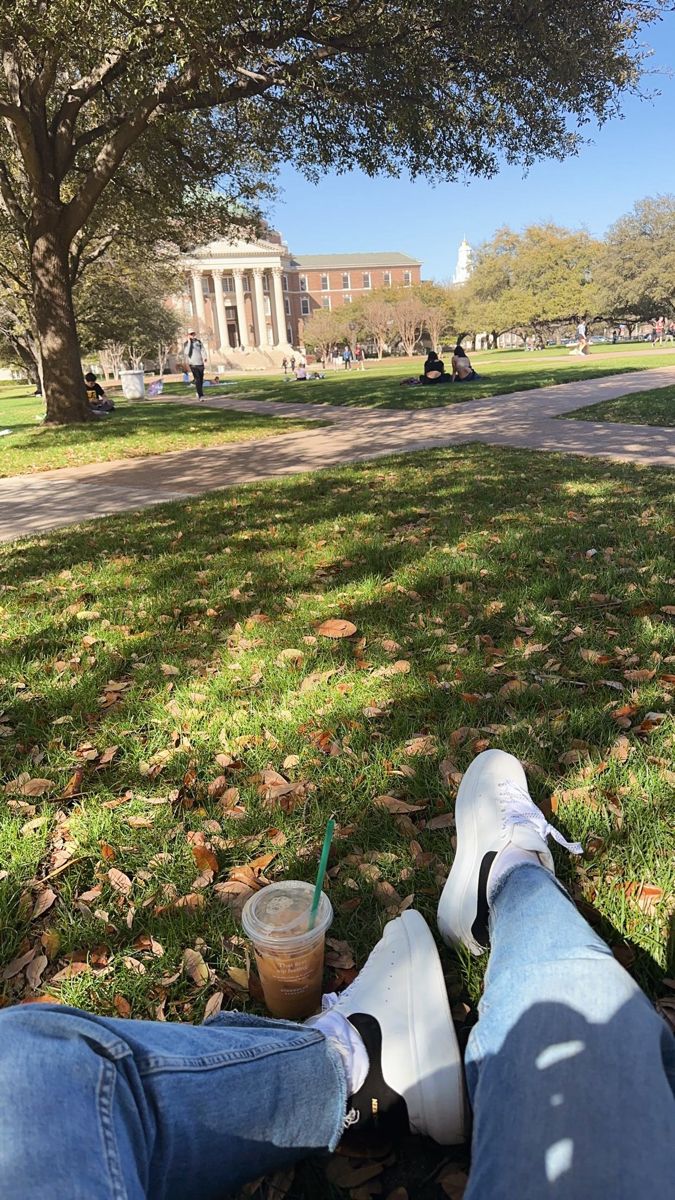 someone is sitting on the grass with their feet up and holding a drink in front of them