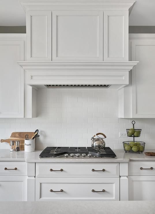 a kitchen with white cabinets and an oven hood over the stove, in front of a counter