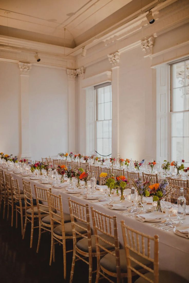 a long table is set up with white linens and floral centerpieces for an event