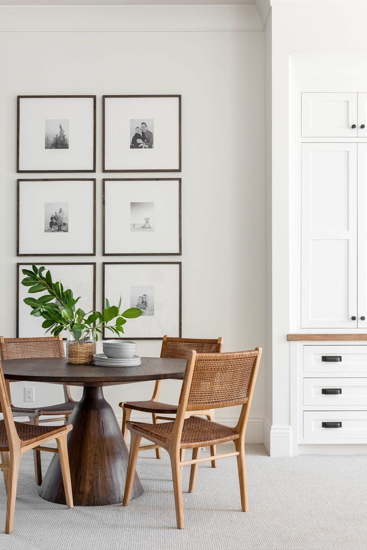 a dining room table with four chairs and pictures on the wall behind it, along with two potted plants