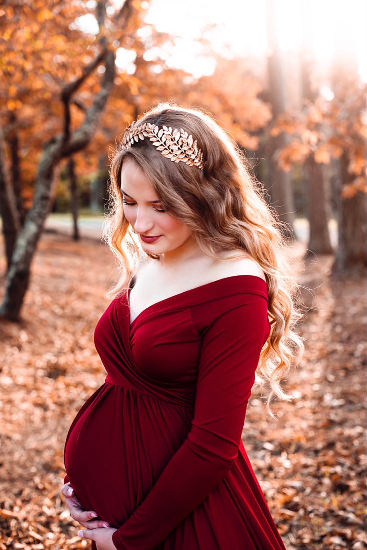 a pregnant woman in a red dress poses for the camera with her hands on her belly