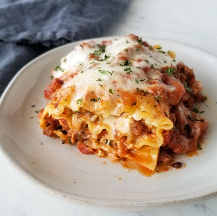 a white plate topped with lasagna covered in sauce and cheese on top of it