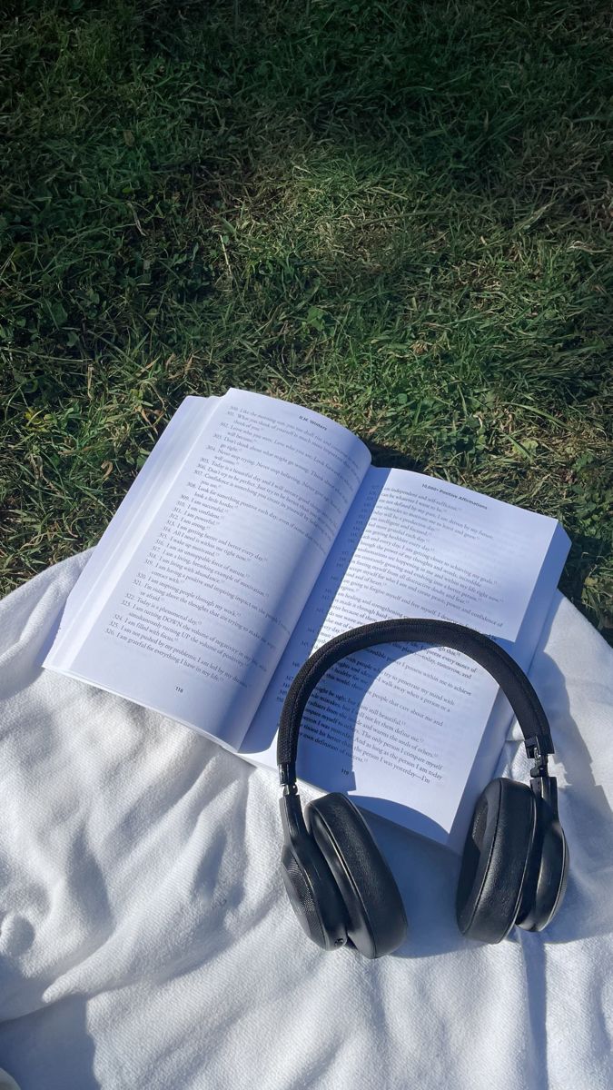 an open book with headphones on top of it sitting on a blanket in the grass