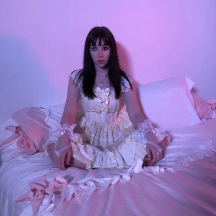 a woman sitting on top of a bed in a white dress