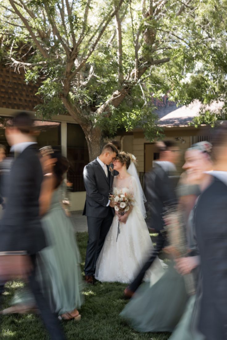 a bride and groom are kissing in front of their wedding party on the grass outside