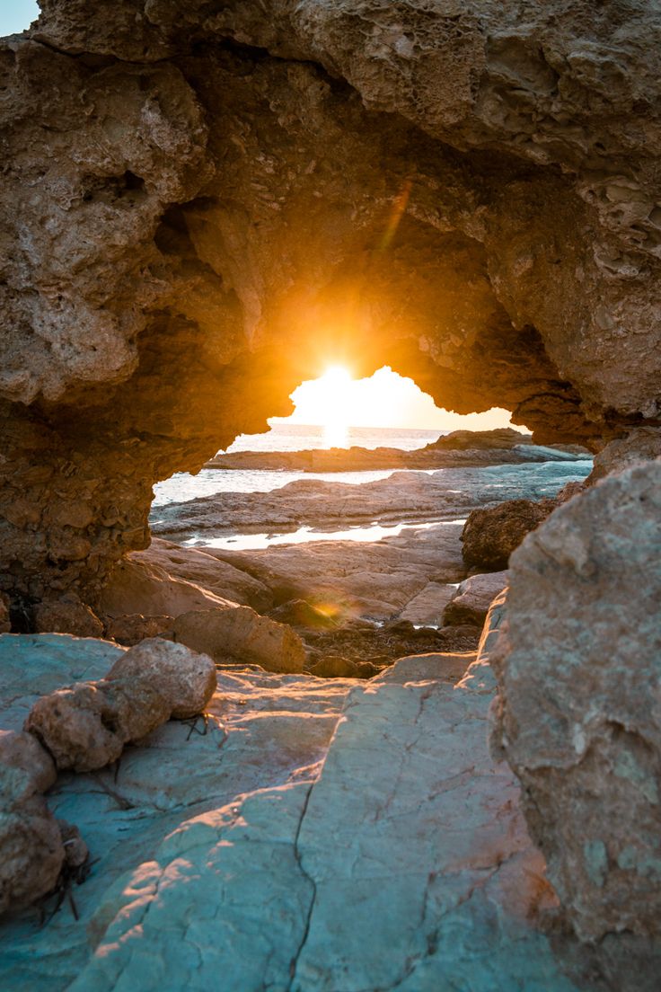 the sun is setting through an arch in the rocks at the ocean's edge