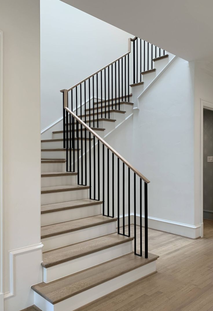 a white staircase with black handrails and wood flooring in an empty room